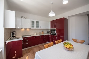 A modern kitchen with white and red cabinets, a built-in oven, and a dining area with a table set for two. - Apartments Villa Anna (Opatija)