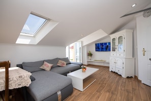 A modern loft apartment with a skylight, grey sofa, white coffee table, and a TV mounted on the wall. - Apartments Villa Anna (Opatija)