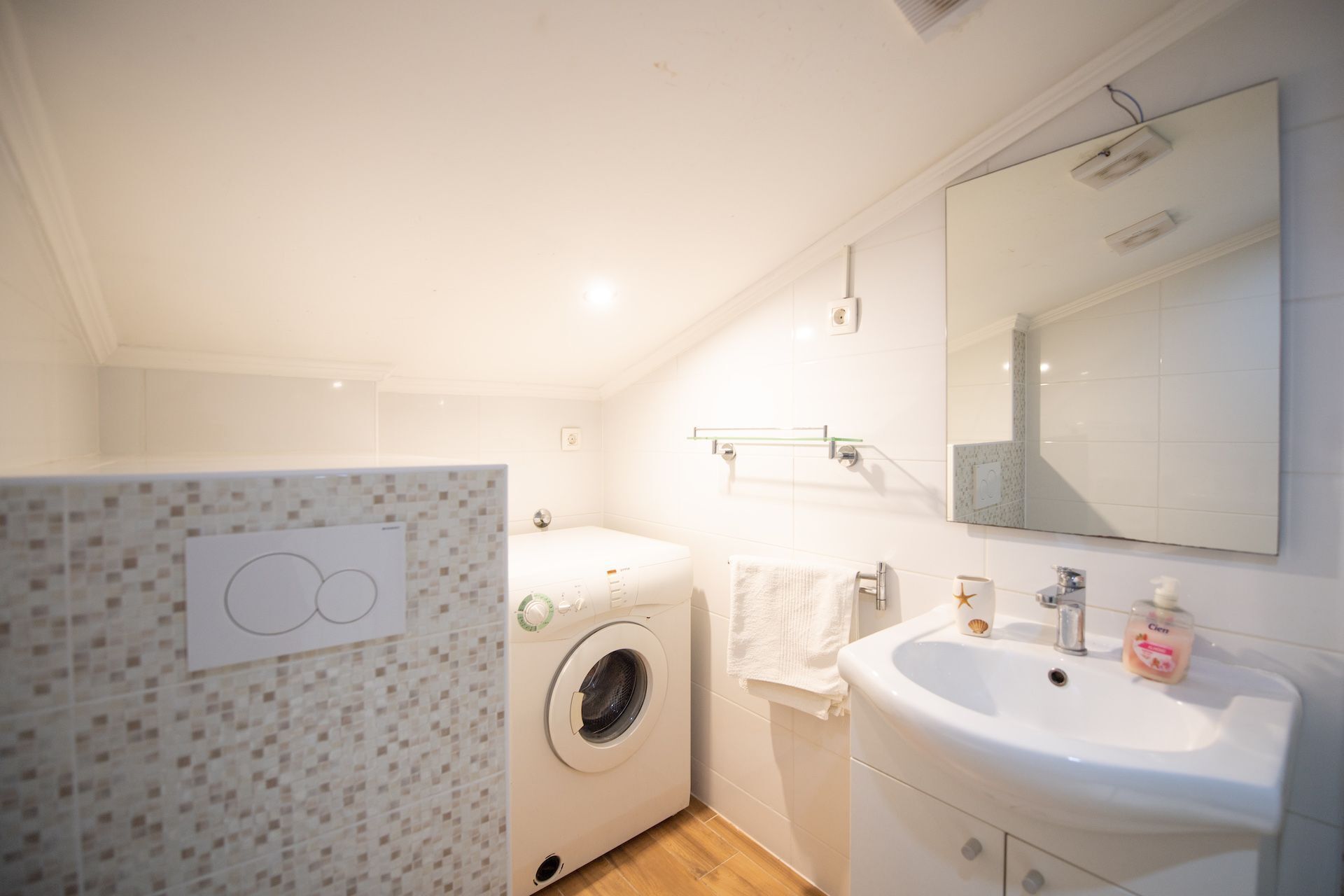 Une salle de bain moderne et compacte, équipée d’un lave-linge, d’un lavabo et d’un miroir.