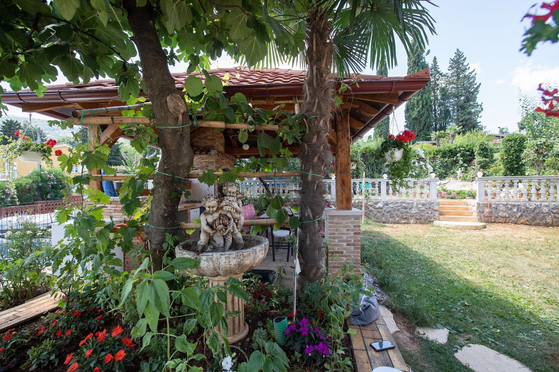 Ein Garten mit einer Pergola, einem Steinklopapfel und einer Statue.