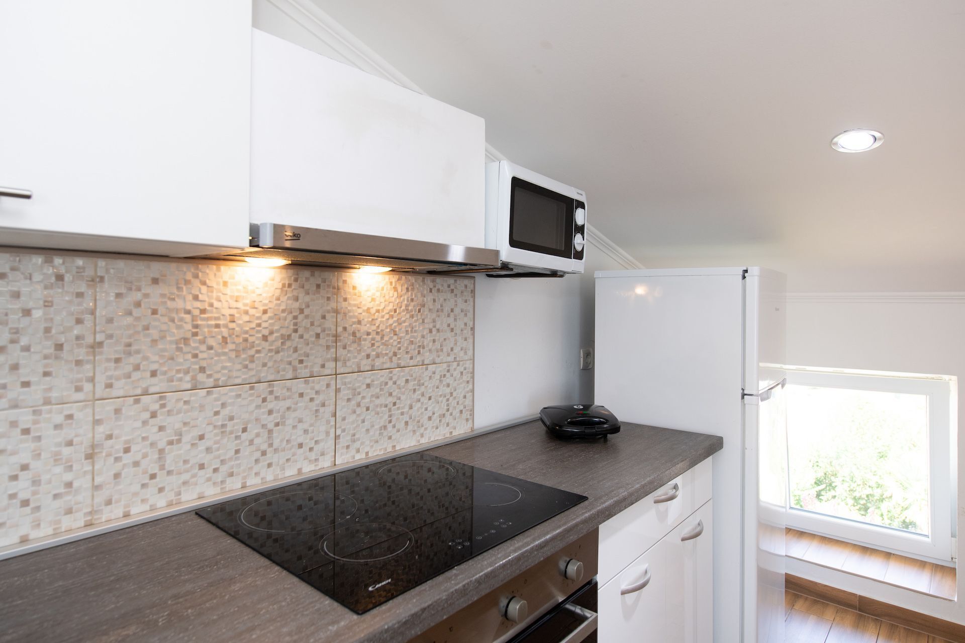 Een moderne keuken met een inbouw inductiekookplaat, een magnetron en een koelkast.