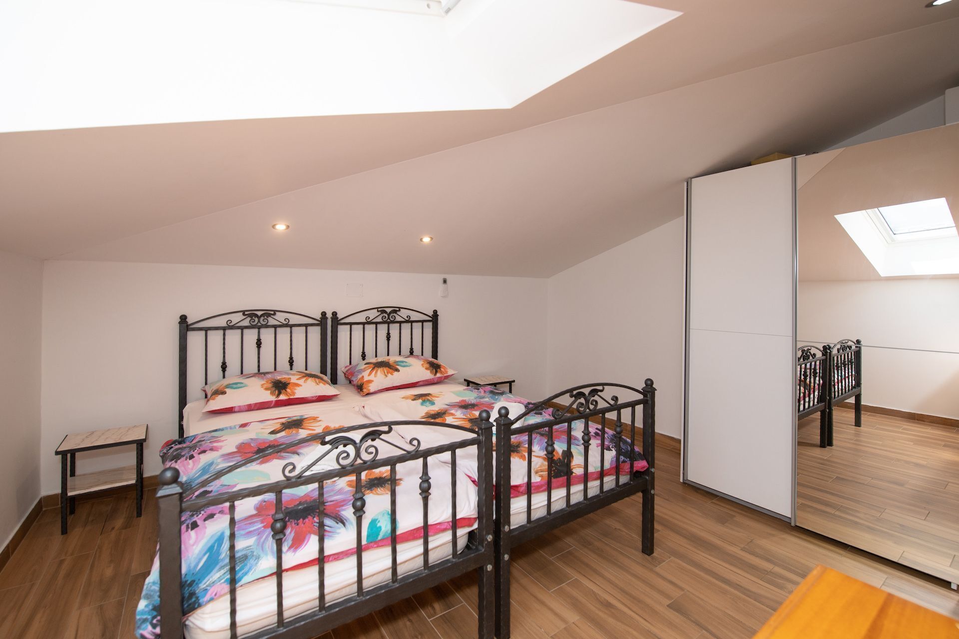 Quarto com cama, mesinha de cabeceira, espelho e claraboia.