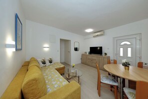 Un soggiorno moderno con un divano, un tavolino in vetro, un tavolo da pranzo con sedie, un televisore piatto e un piccolo mobiletto.