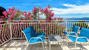 Un balcon doté de balustrades en métal blanc, de deux chaises bleues avec des coussins et d’une petite table.