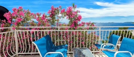 A balcony with white metal railings, two blue cushioned chairs, and a small table.