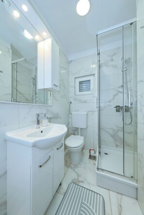 Un bagno moderno con cabina doccia in vetro, lavandino bianco e water.