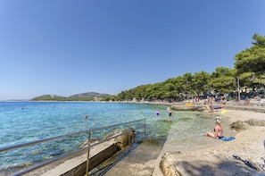 A beach with clear water, a rocky shore, and people swimming and relaxing. - Apartment Zamalin Seaview (Tribunj)