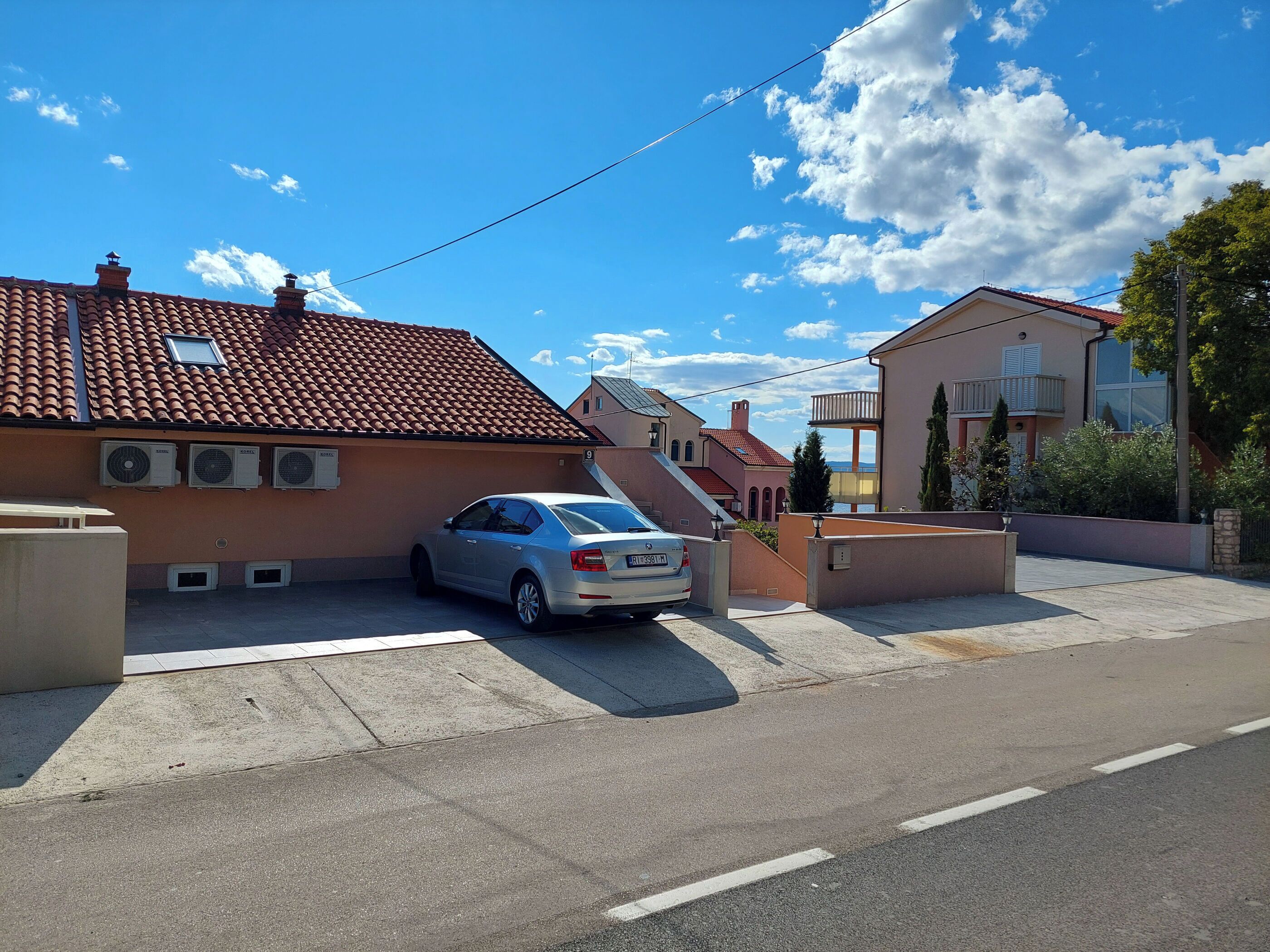 Une rue résidentielle bordée de maisons, avec une voiture garée et un ciel bleu dégagé.