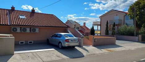 Une rue résidentielle bordée de maisons, avec une voiture garée et un ciel bleu dégagé.