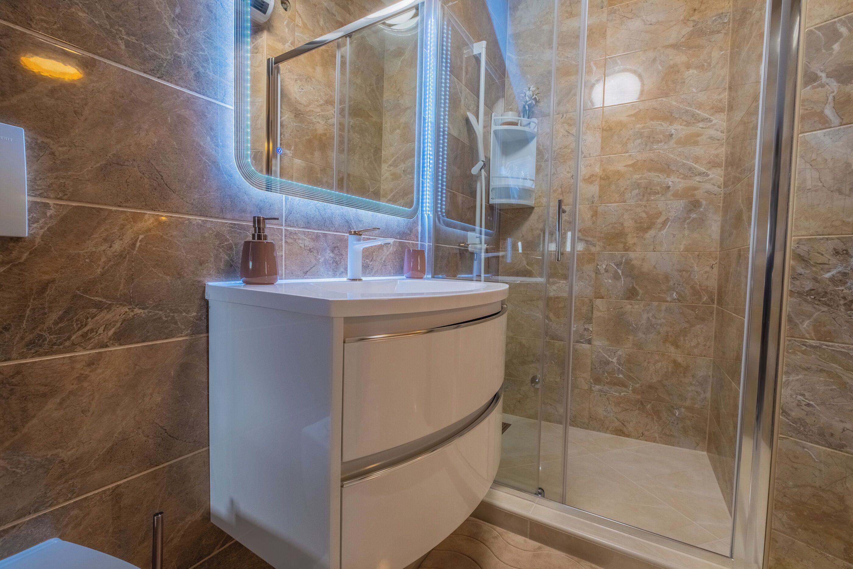 Een moderne badkamer met een gebogen wit badkamermeubel, een glazen douchecabine en marmeren wanden.