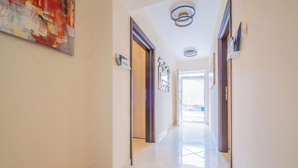 Een schone, moderne hal met een postkantoorbord, een moderne lamp en een doorkijk naar een andere kamer.