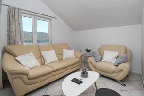 Ein Wohnzimmer mit einer Couch, einem Sessel, einem kleinen Tisch und einer Fernbedienung.