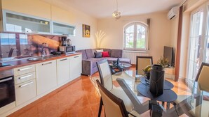 Una cucina moderna con mobili bianchi, una zona pranzo con tavolo in vetro e un accogliente soggiorno con divano e camino.