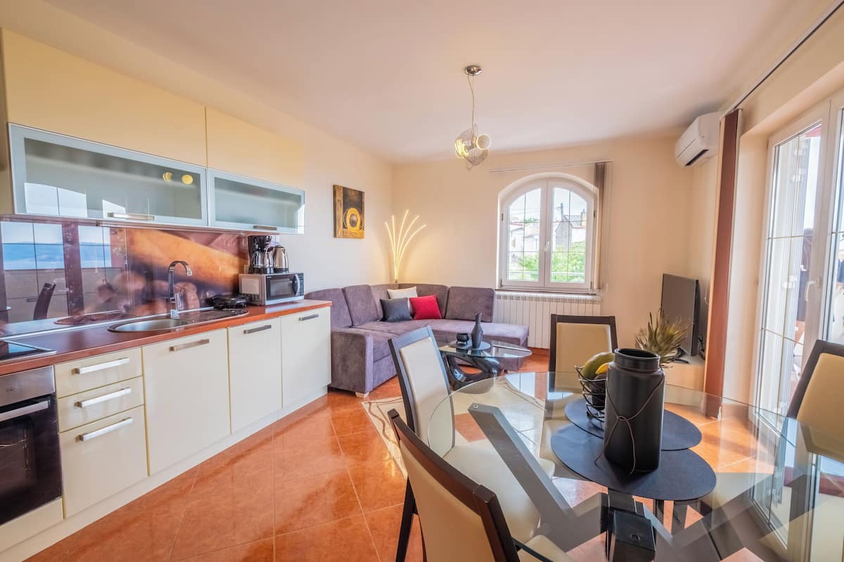 A modern kitchen with white cabinets, a dining area with a glass table, and a cozy living space with a sofa and a fireplace.
