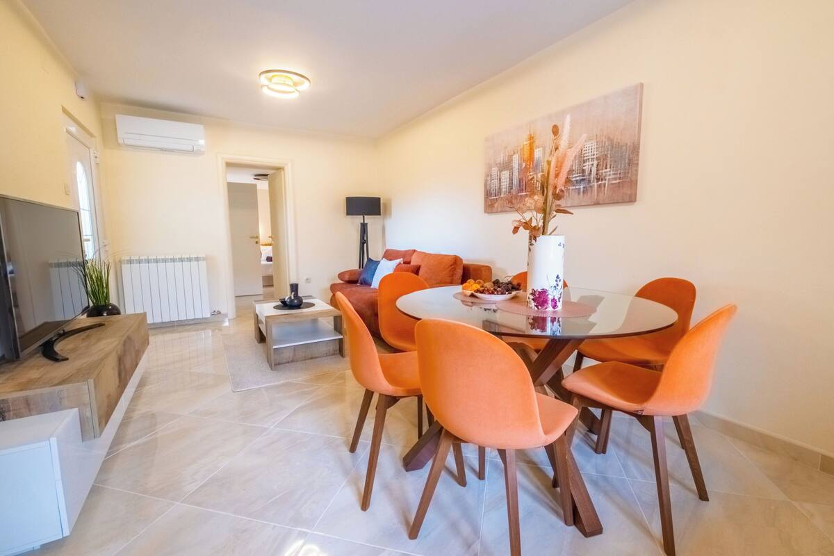 A modern dining area with a round table, orange chairs, and a vase of flowers.