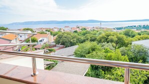 Un balcone con ringhiera metallica che si affaccia su una zona residenziale con case e uno specchio d'acqua in lontananza.