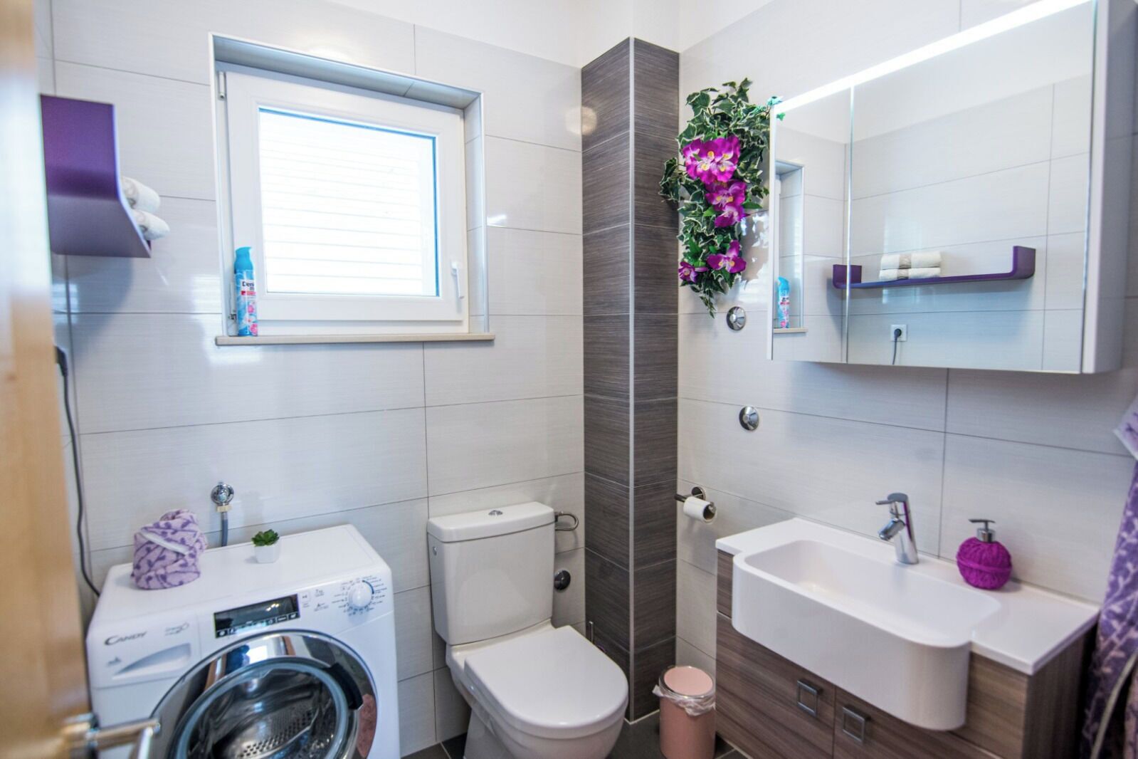 A modern bathroom with a washing machine, toilet, sink, and a window.