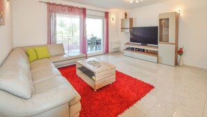 A modern living room with a white sofa, a red rug, a TV, and a cabinet. - Apartment Ray of Sunshine (Pasman)