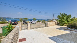 A coastal property with a paved driveway leading to a gated entrance, a parked car, and a motorcycle. - Apartment Ray of Sunshine (Pasman)