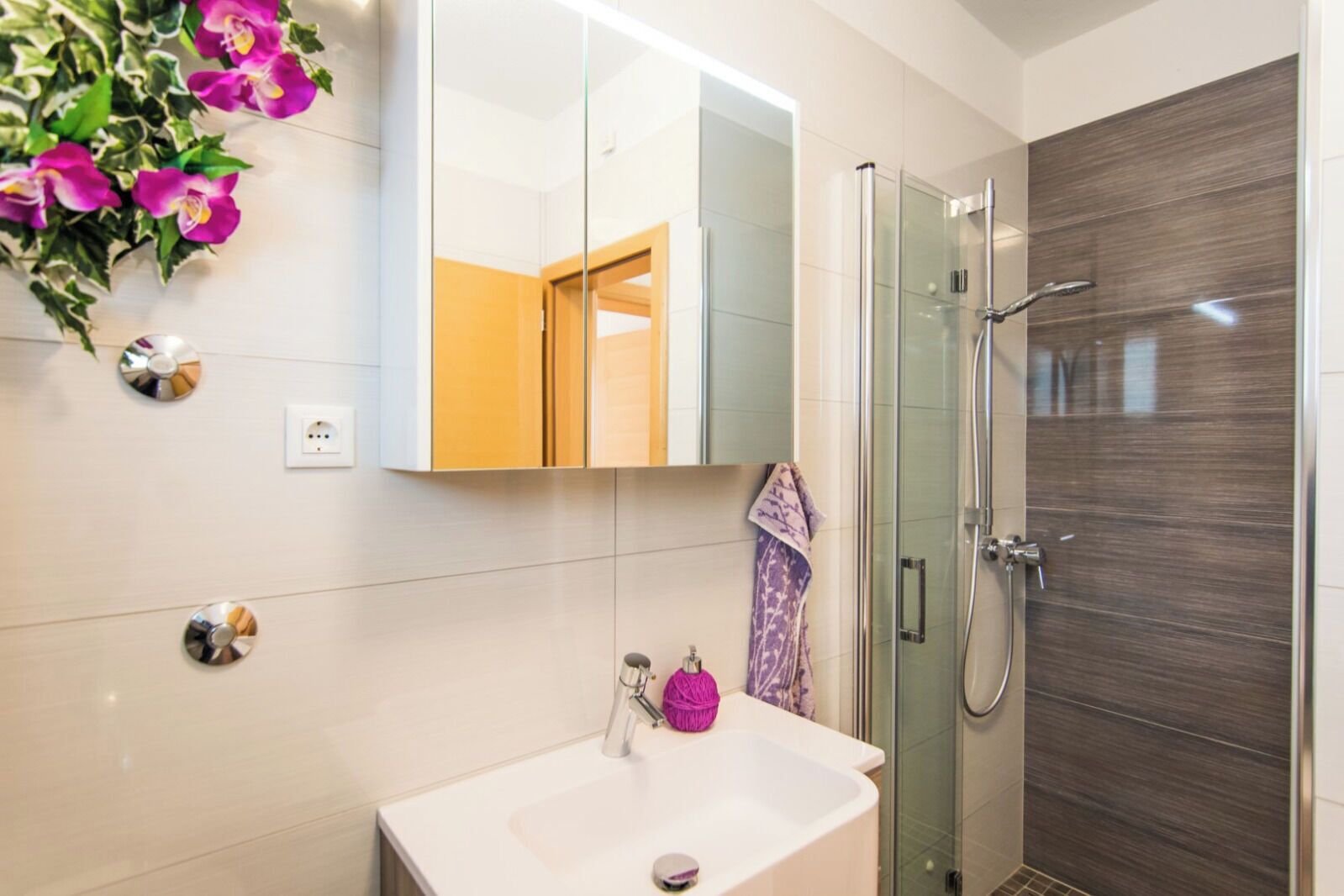 A bathroom with a glass shower, a white sink, and a mirror.