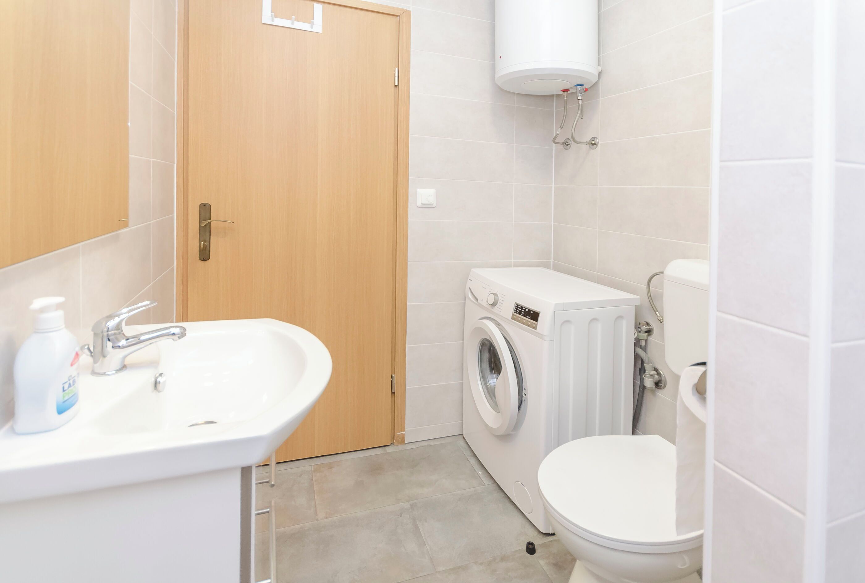 Ein kleines, sauberes Badezimmer mit Waschbecken, Waschmaschine und Toilette.