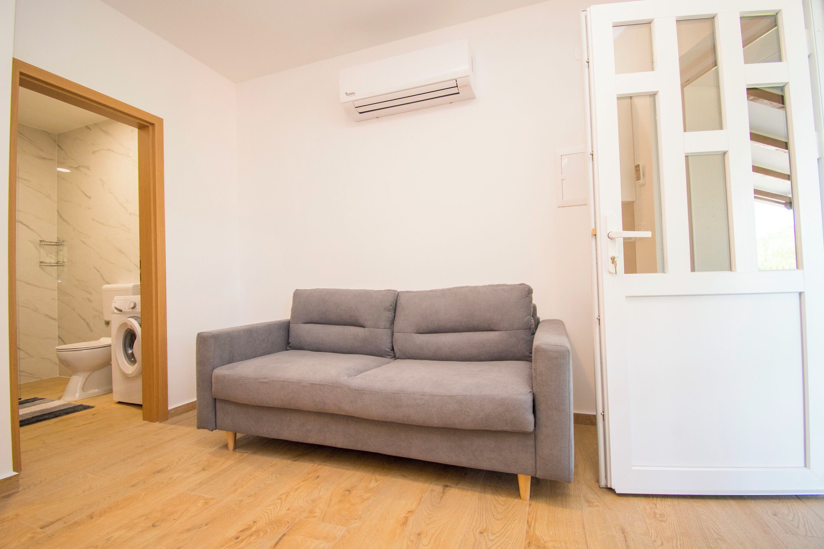 A room with a grey sofa, a washing machine, and a white door with glass panels.