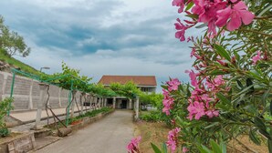 Ein Weg führt zu einem Gebäude mit roten Ziegeldach, umgeben von Grünpflanzen und rosa Blüten.