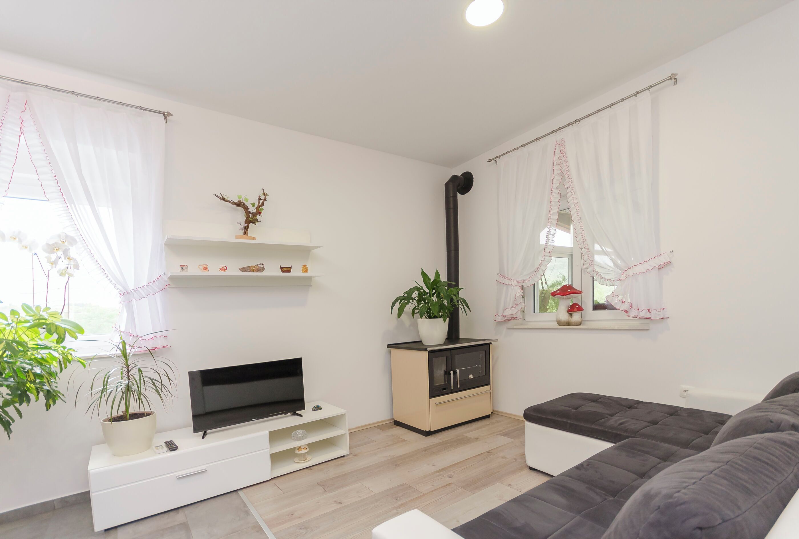 Una sala moderna con un televisor de pantalla plana, un sofá, un mueble con una planta y una ventana con cortinas.