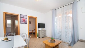 A living room with a dining table, chairs, a sofa, a TV, and a window with curtains. - Apartment Monika (Vodice)