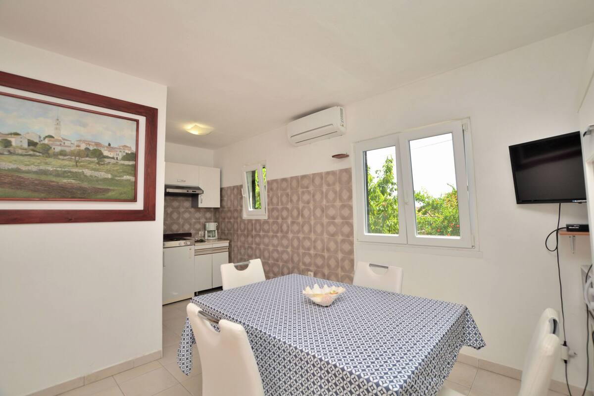 A dining area with a table set for two, a painting on the wall, and a kitchen in the background.