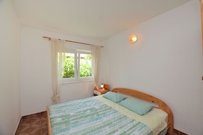 Een slaapkamer met een bed, een raam met gordijnen, een nachtkastje en een wandlamp.