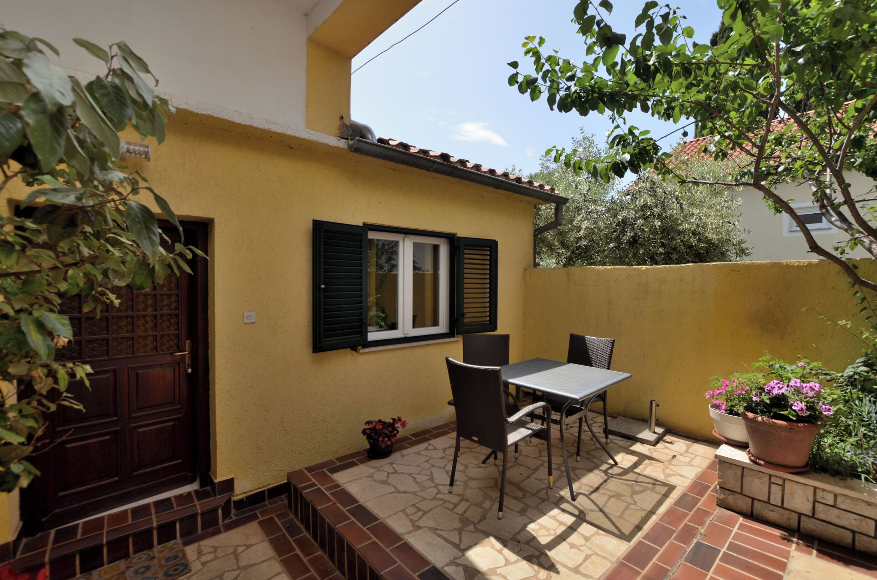 A small patio with a table and chairs, a door, and potted plants.
