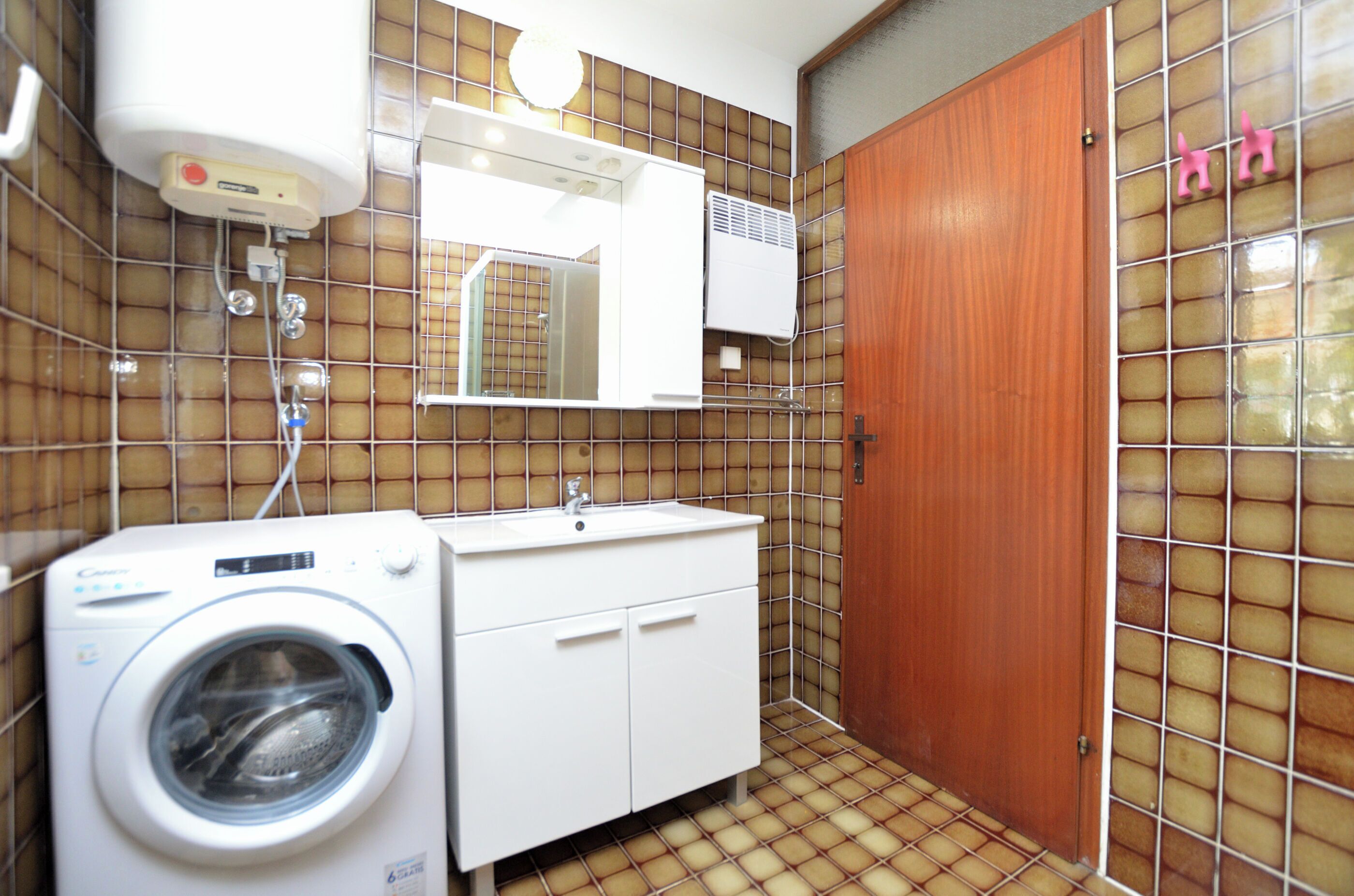 A compact bathroom with a washing machine, a sink, and a mirror.
