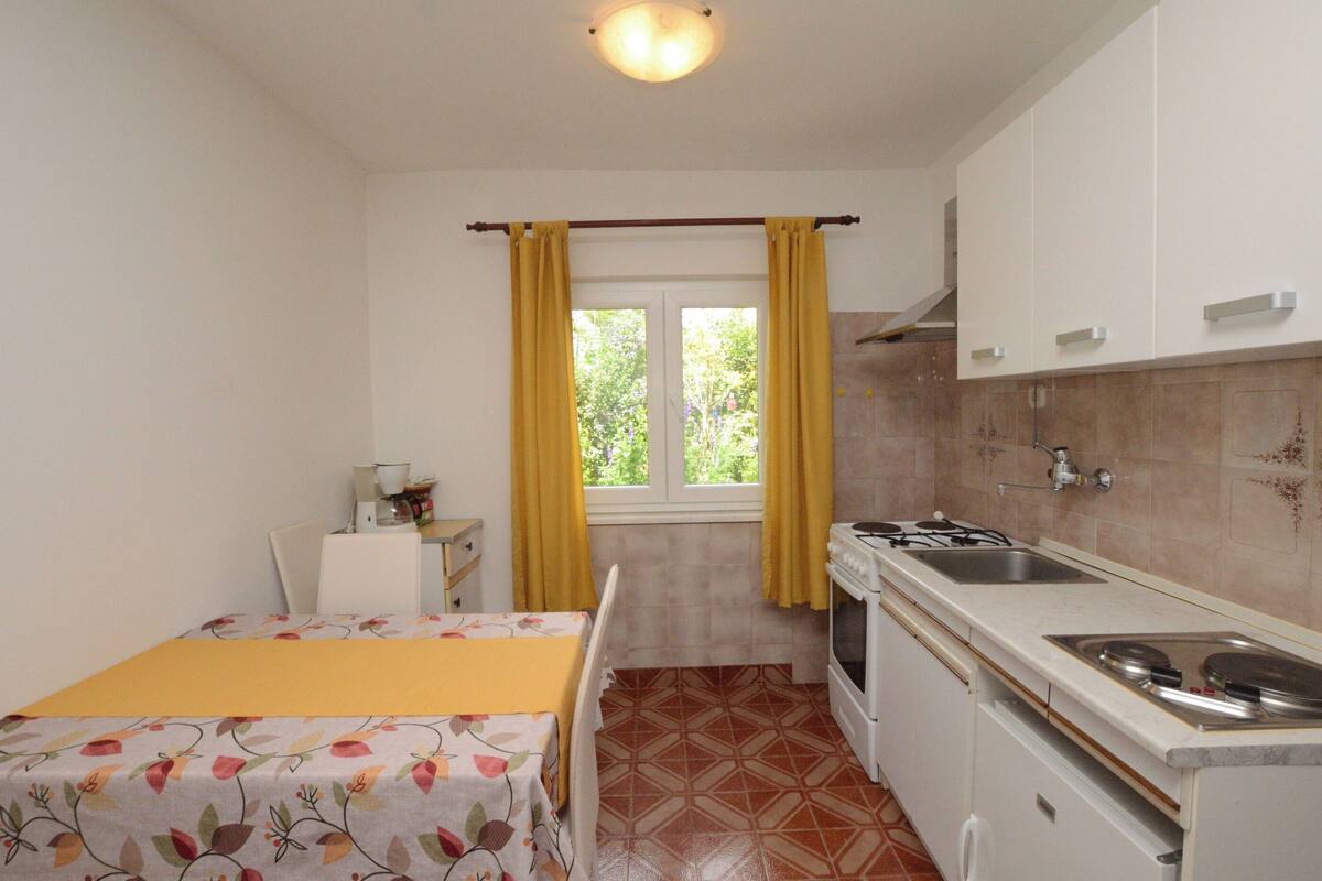 A compact kitchen with a stove, sink, and a window with yellow curtains.