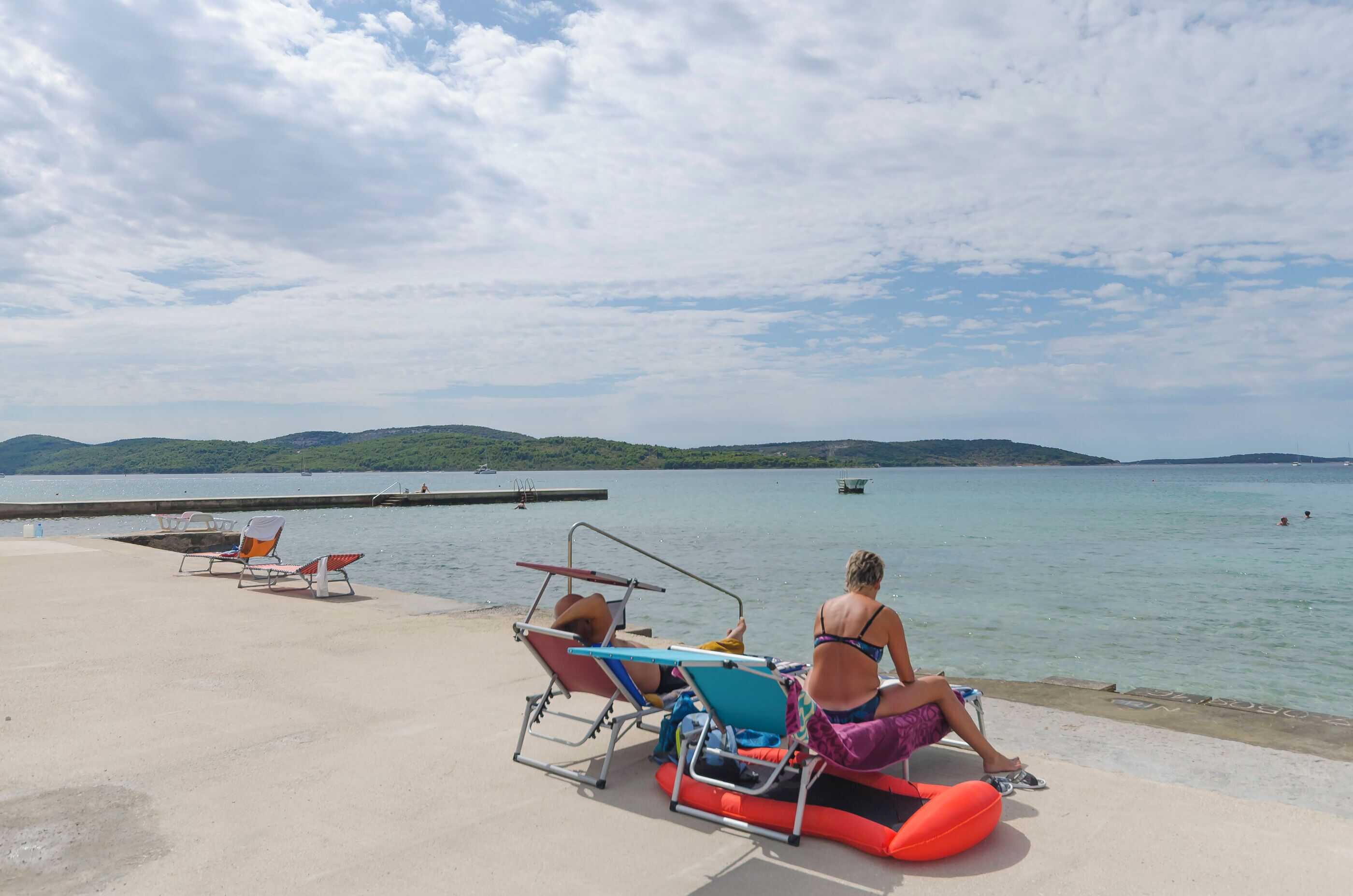A beachside area with lounge chairs and a dock extending into calm waters.