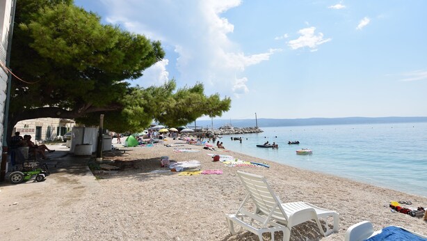 Una spiaggia con una fila di sedie bianche, una tenda e persone che si rilassano.
