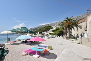 Una spiaggia con ombrelloni, asciugamani e una collina rocciosa sullo sfondo.