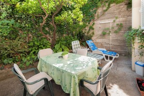 Un piccolo patio con tavolo e sedie, circondato da rigogliosa vegetazione e un muro.