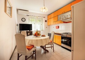 Una cucina compatta con zona pranzo, dotata di fornello, forno e tavolo apparecchiato con frutta e teiera.