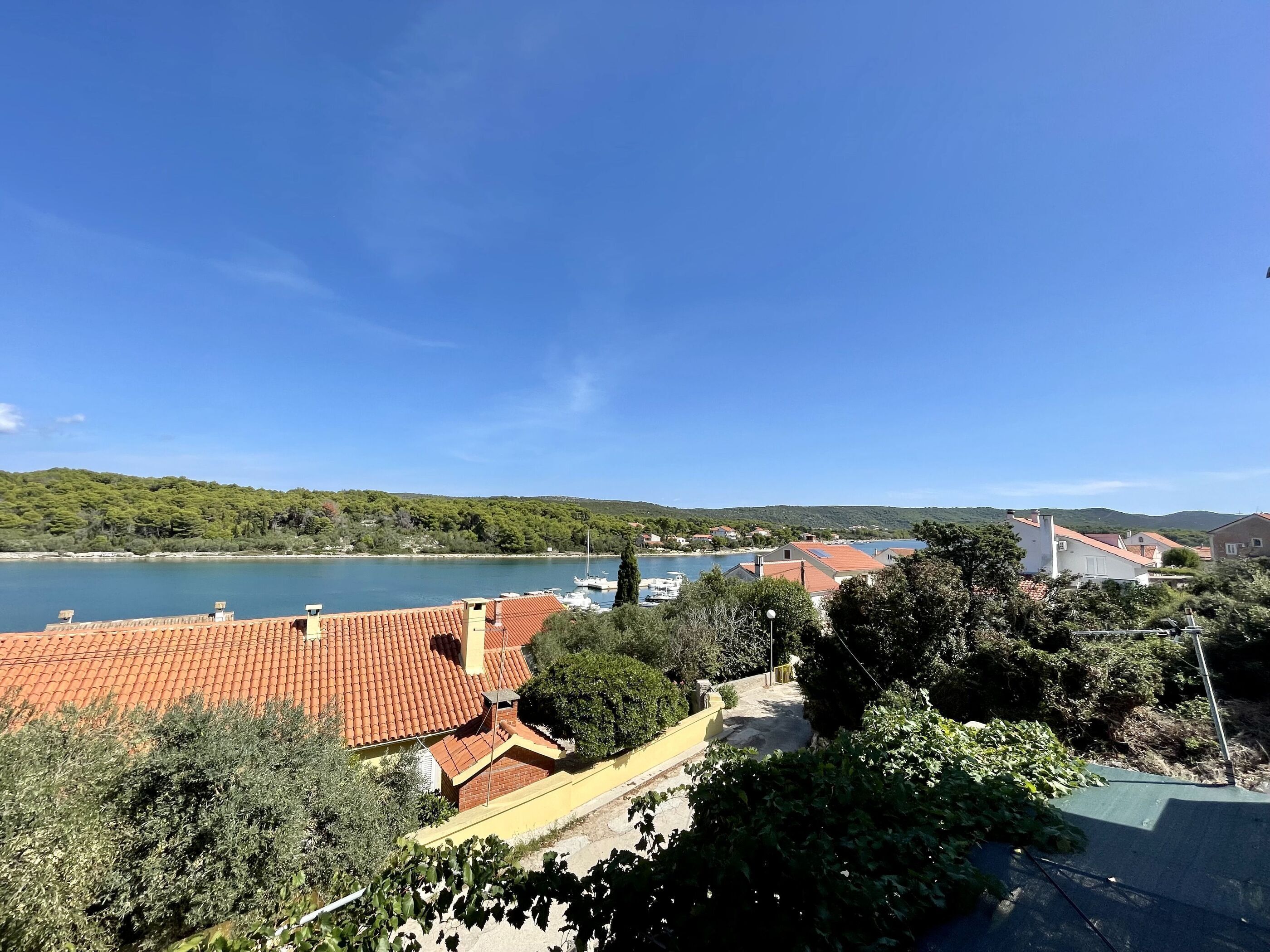 Un pueblo costero con edificios de tejas de color terracota, un puerto deportivo con barcos y colinas verdes al fondo.