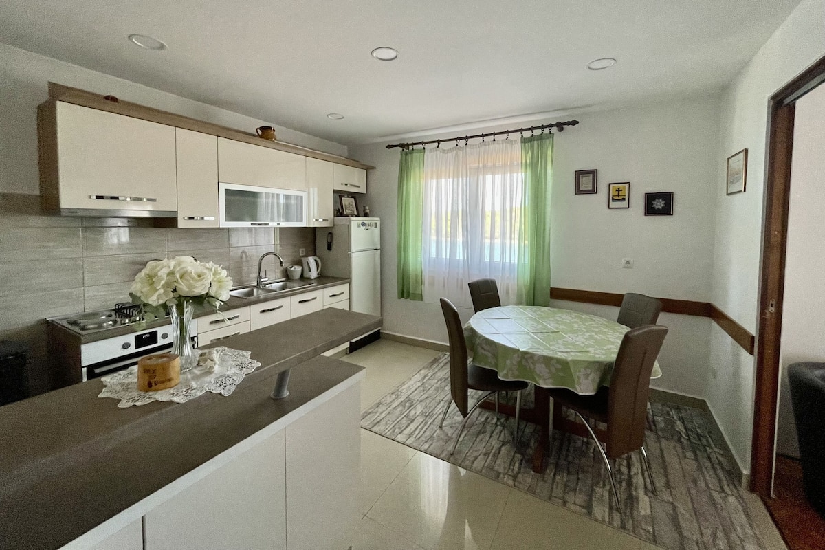 A modern kitchen with white cabinets, a dining table with chairs, and a green curtain.