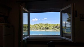 A room with an open window overlooking a lake and forested hills. - Apartments Veli Rat (Sali)