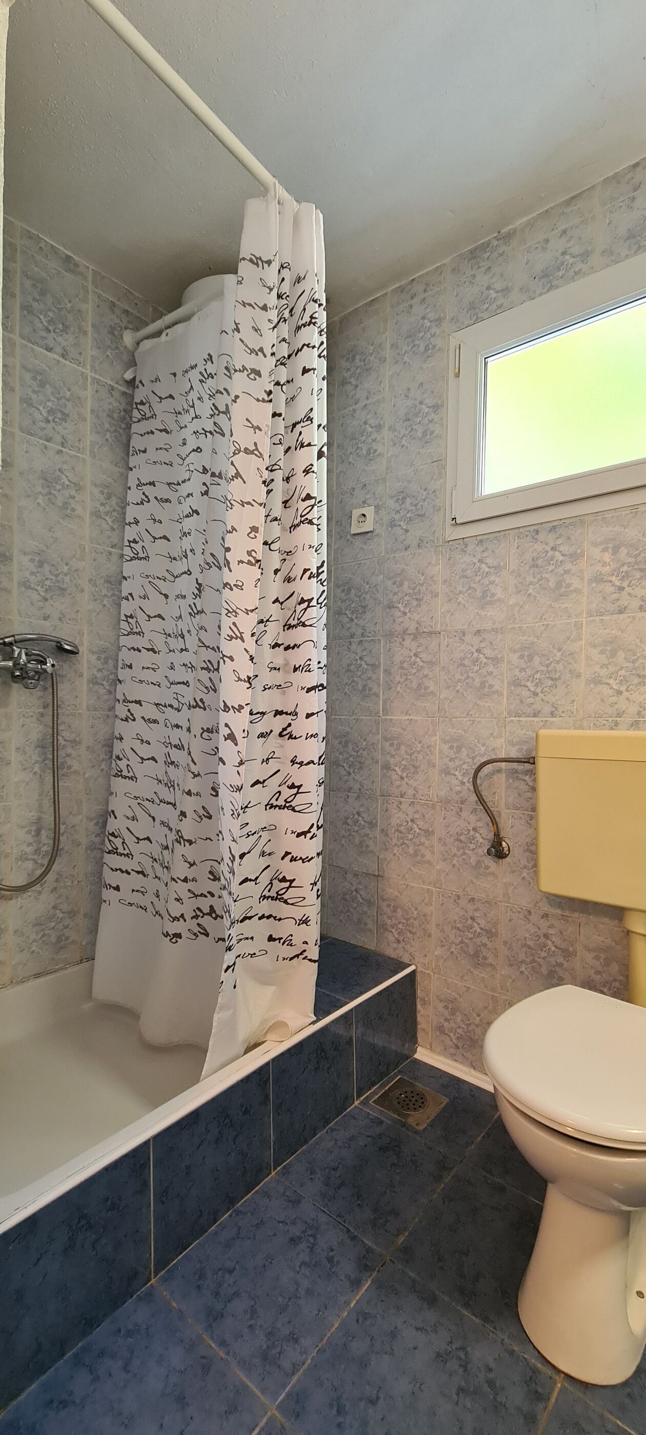 A bathroom with a shower curtain covered in signatures, a toilet, and a window above the sink.