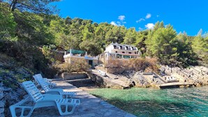 A coastal property with a stone pathway leading to a pool, surrounded by lush greenery and a large building with multiple balconies. - Apartments On the Beach (Sucuraj)