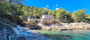 A coastal property with a stone pathway leading to a pool, surrounded by lush greenery and a large building with multiple balconies. - Apartments On the Beach (Sucuraj)