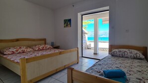 A room with two beds, one larger and one smaller, both with wooden frames and patterned bedding. There is a door leading to an outdoor area with a view of the sea. - Apartments On the Beach (Sucuraj)