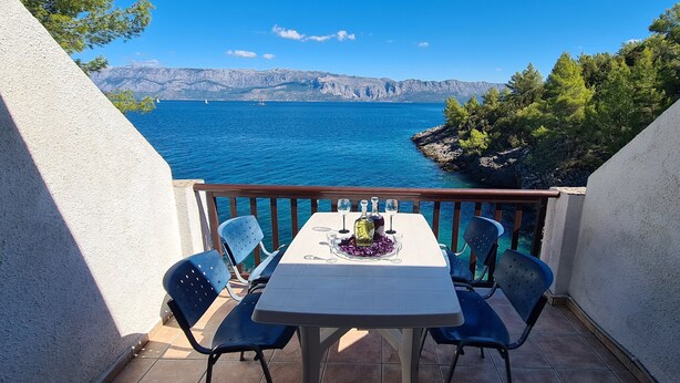 A balcony with a table set for two, overlooking a body of water and a mountainous landscape. - Apartments On the Beach (Sucuraj)