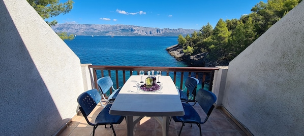 A balcony with a table set for two, overlooking a body of water and a mountainous landscape. - Apartments On the Beach (Sucuraj)