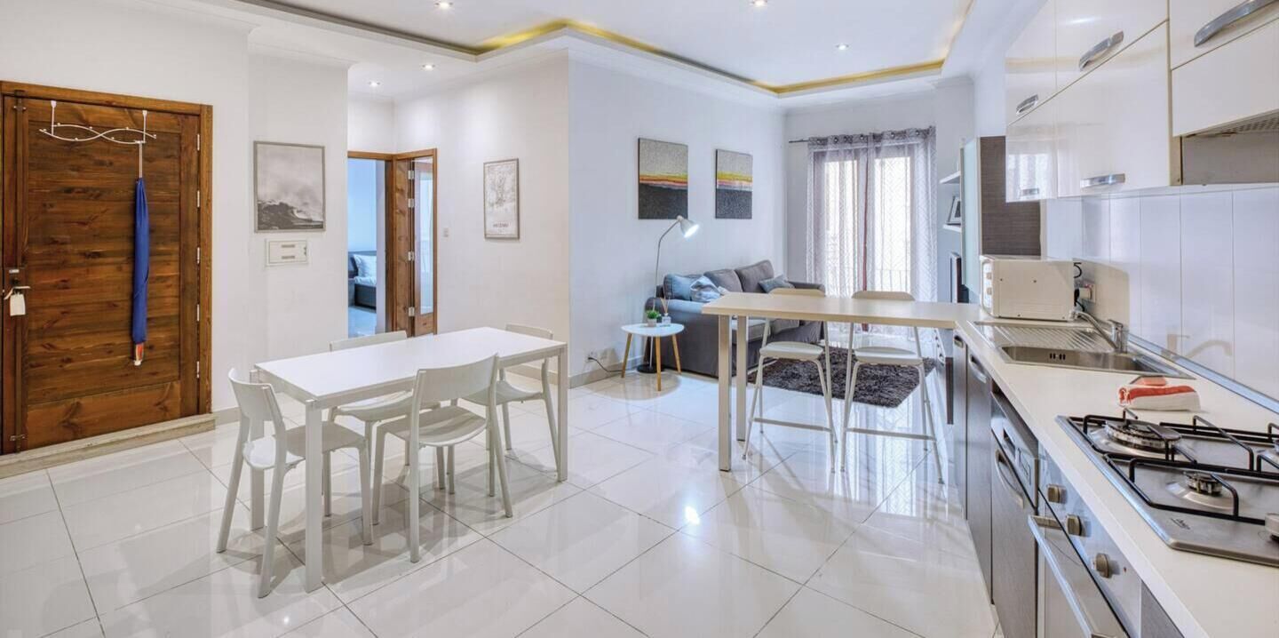 Una cucina moderna con mobili bianchi, piano cottura a gas e zona pranzo con tavolo e sedie bianche.