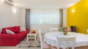 A room with a red sofa, a white table, a round dining table, and a yellow wall. - Apartment Burica (Primosten)